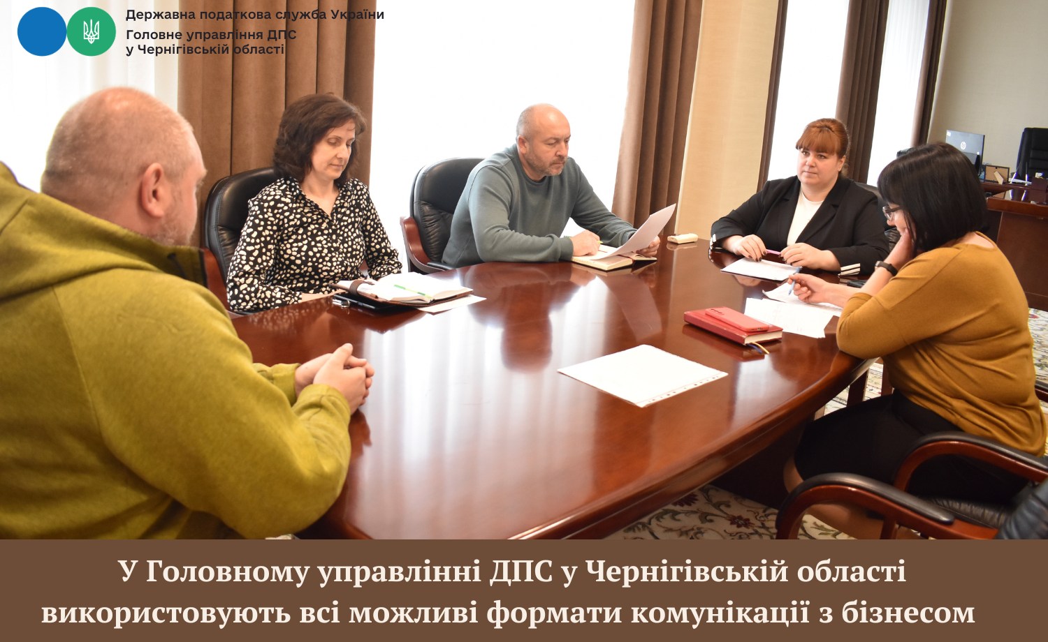 Фотографія чоловіки й жінки сидять за овальним столом, один із них тримає документи на аркушах