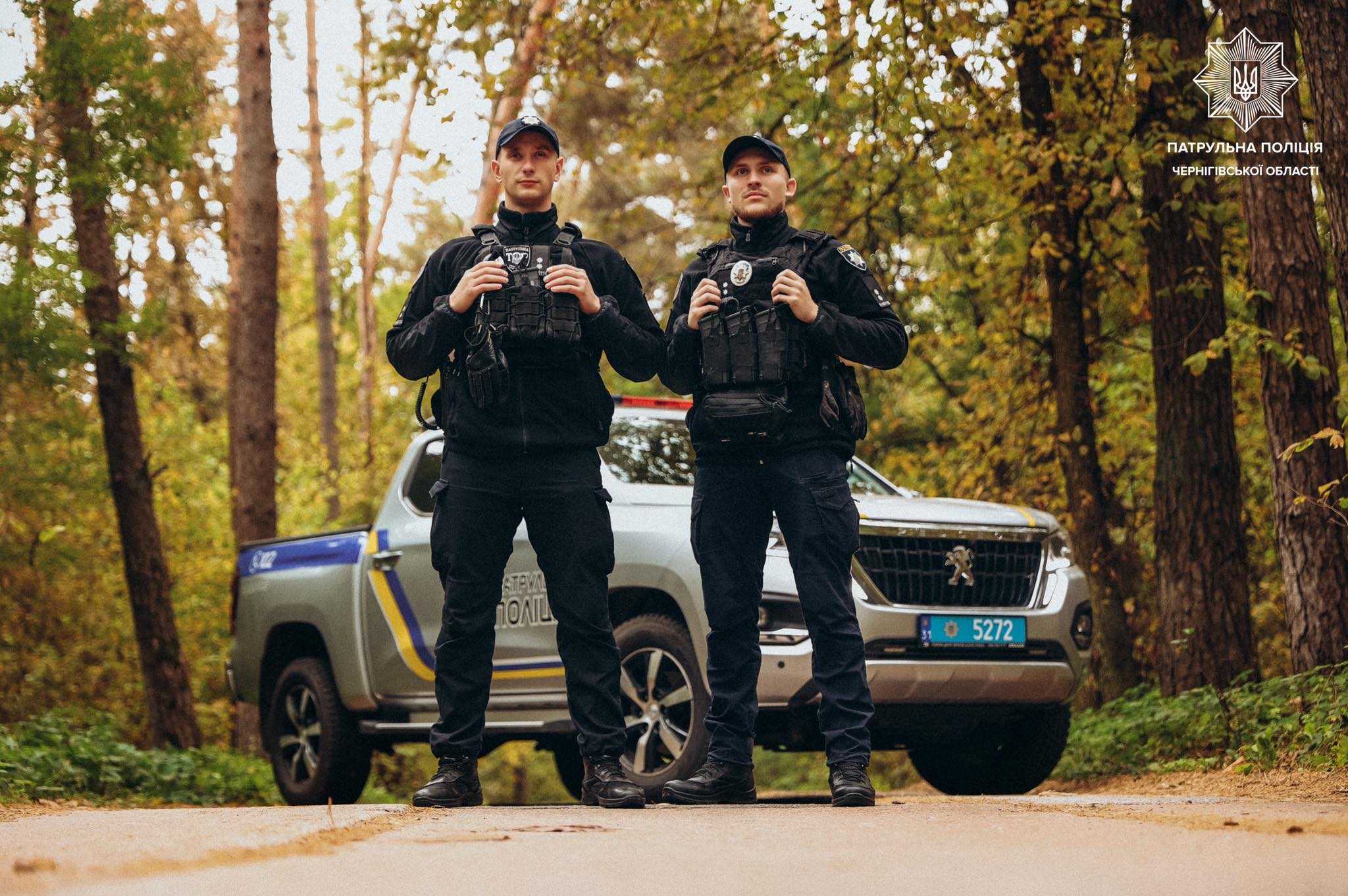 Фотографія два патрульних поліцейських на дорозі, ползаду в них машина й ліс