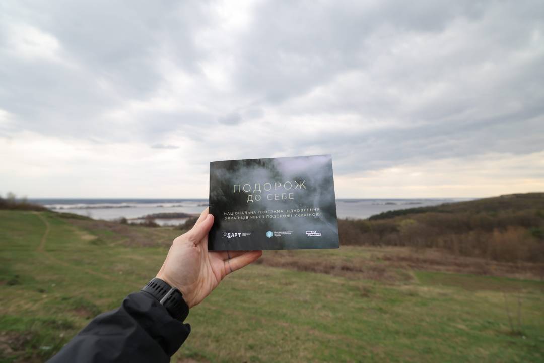 Фотографія рука тримає картинку на тлі рівнинного пейзажу